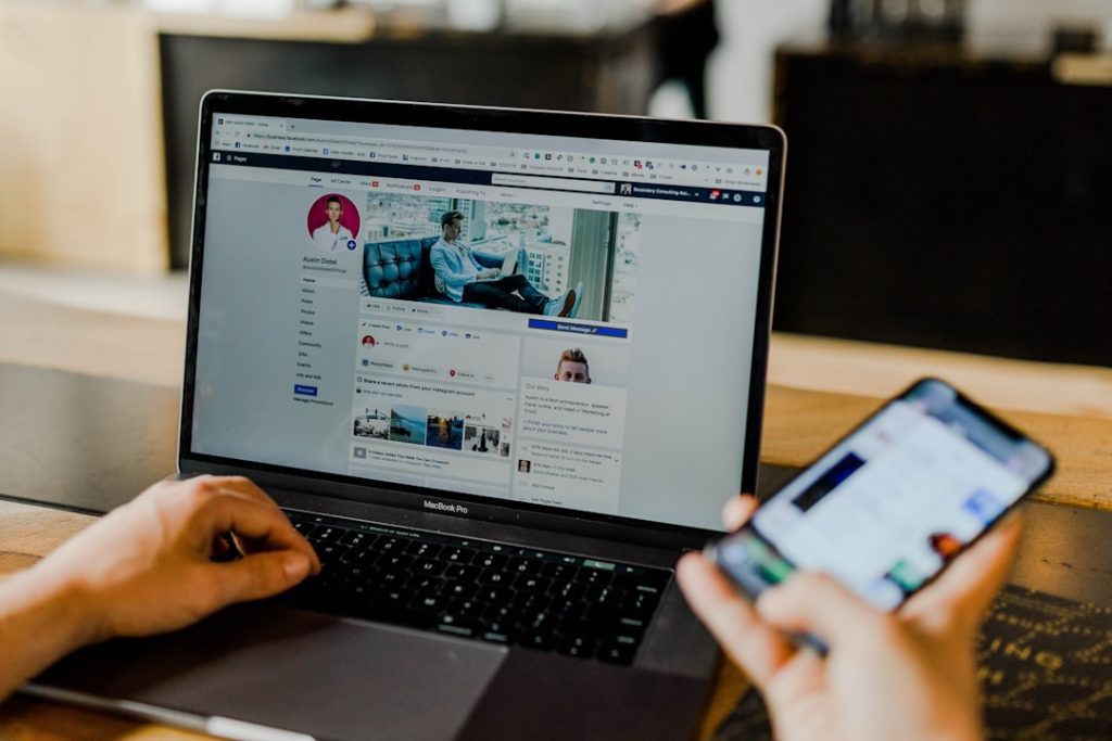 person-using-both-laptop-and-smartphone-tlzhfrlj6ny Facebook page of an entrepreneurs social media on desktop and mobile.